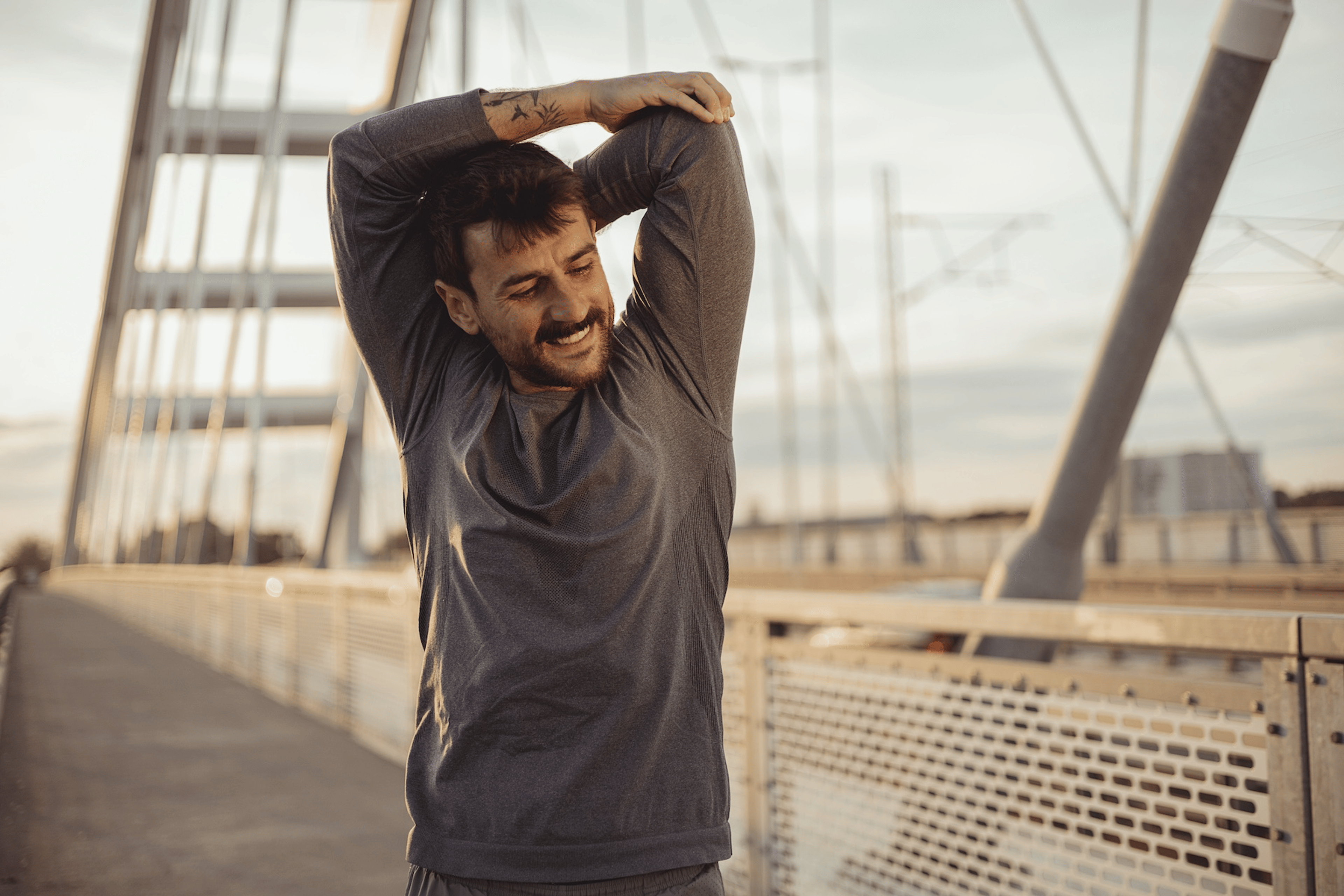 A man smiling and stretching his arms before going on an outdoor run in the morning.