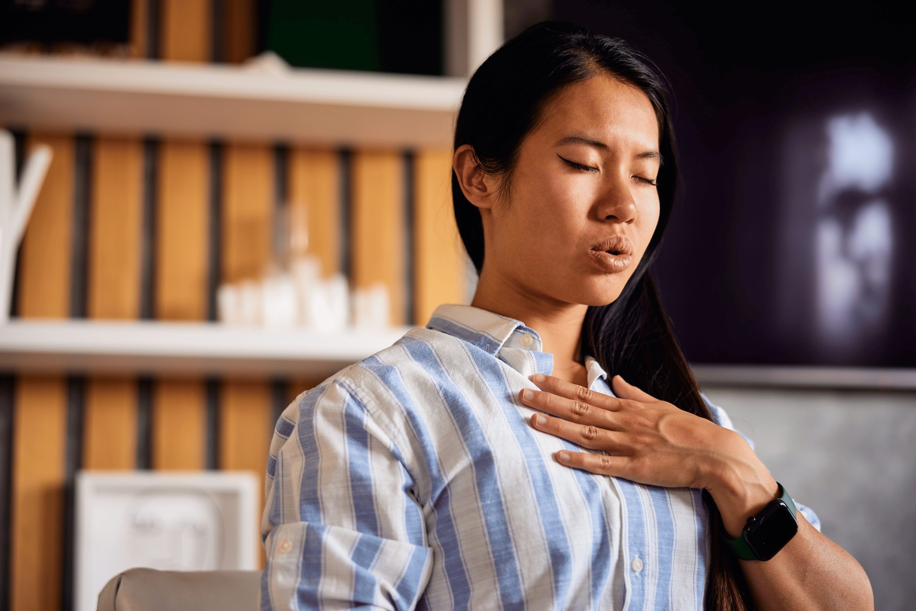A woman breathing out through her mouth while practicing cyclic sighing. Her hand is resting on her chest.