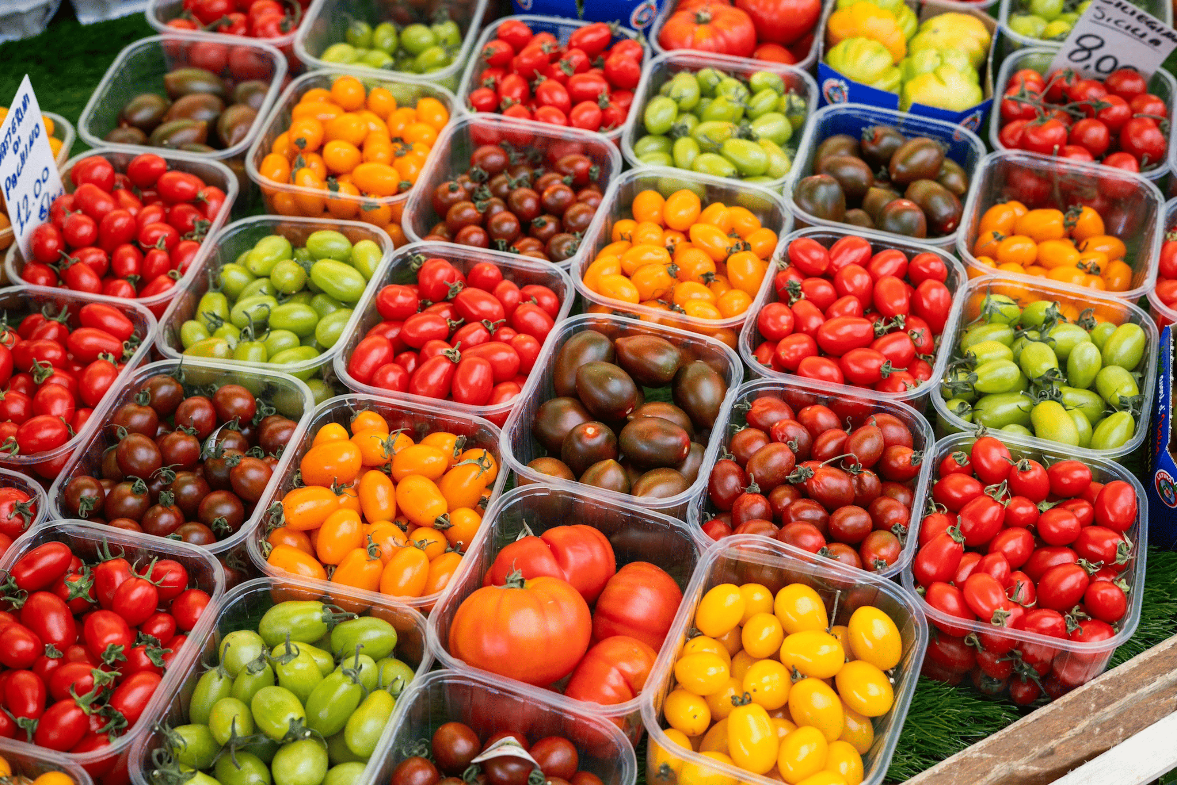 A farmer's market table full of colorful tomato cartons. Tomatoes are hydrating foods.