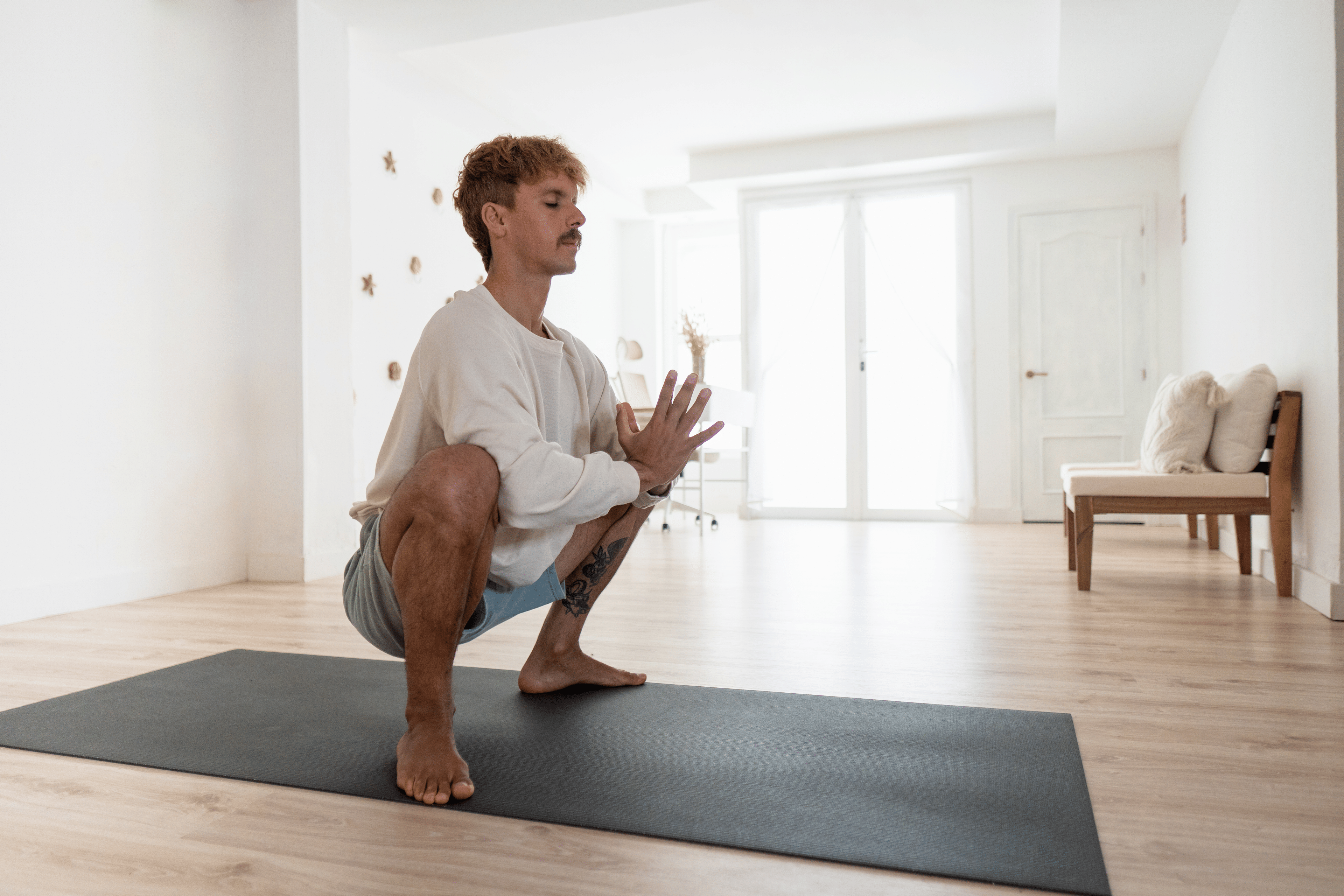 Man practicing Garland Pose (Malasana or Yoga Squat) during a Peloton yoga class at home.