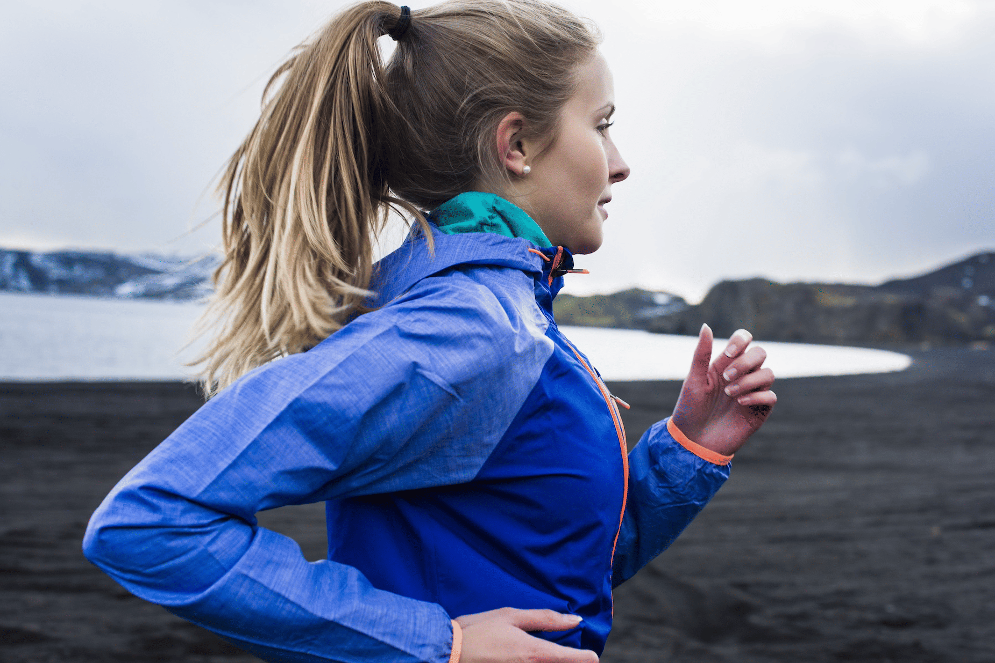 A side-view photo of a woman running outside on a chilly day.