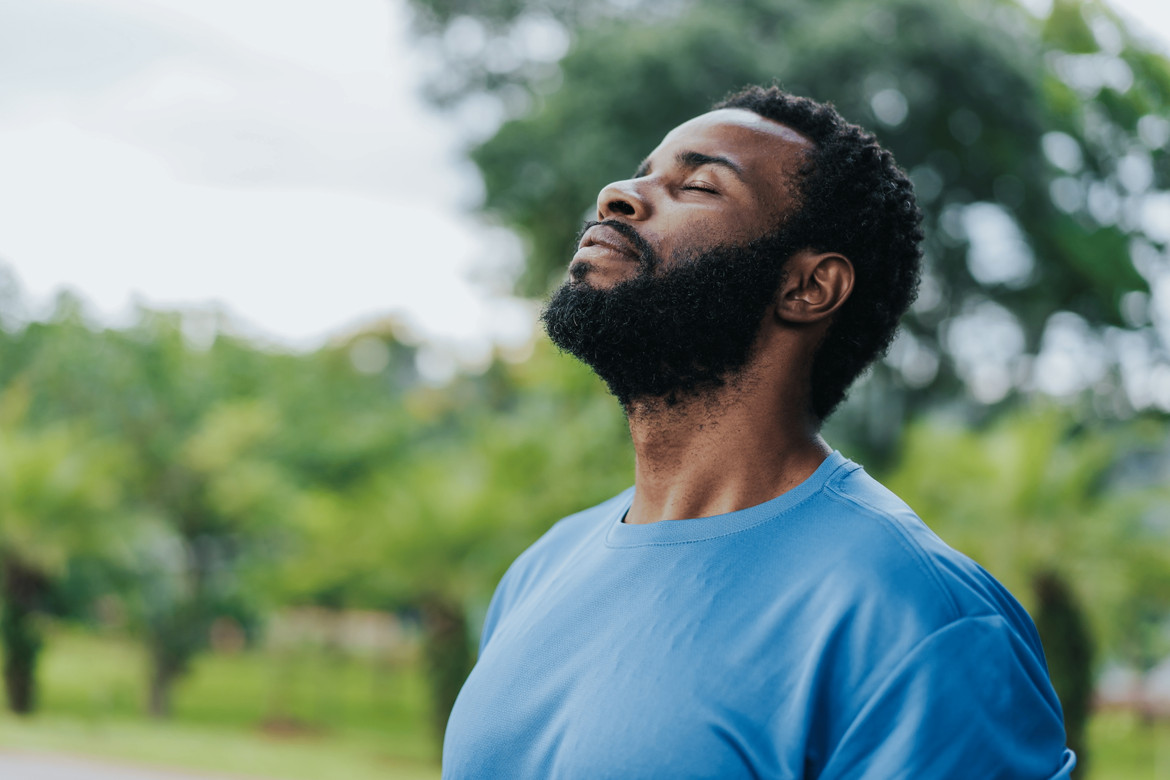 A man meditating outside, looking up while closing his eyes. Learn more about meditating before or after a workout in this article.