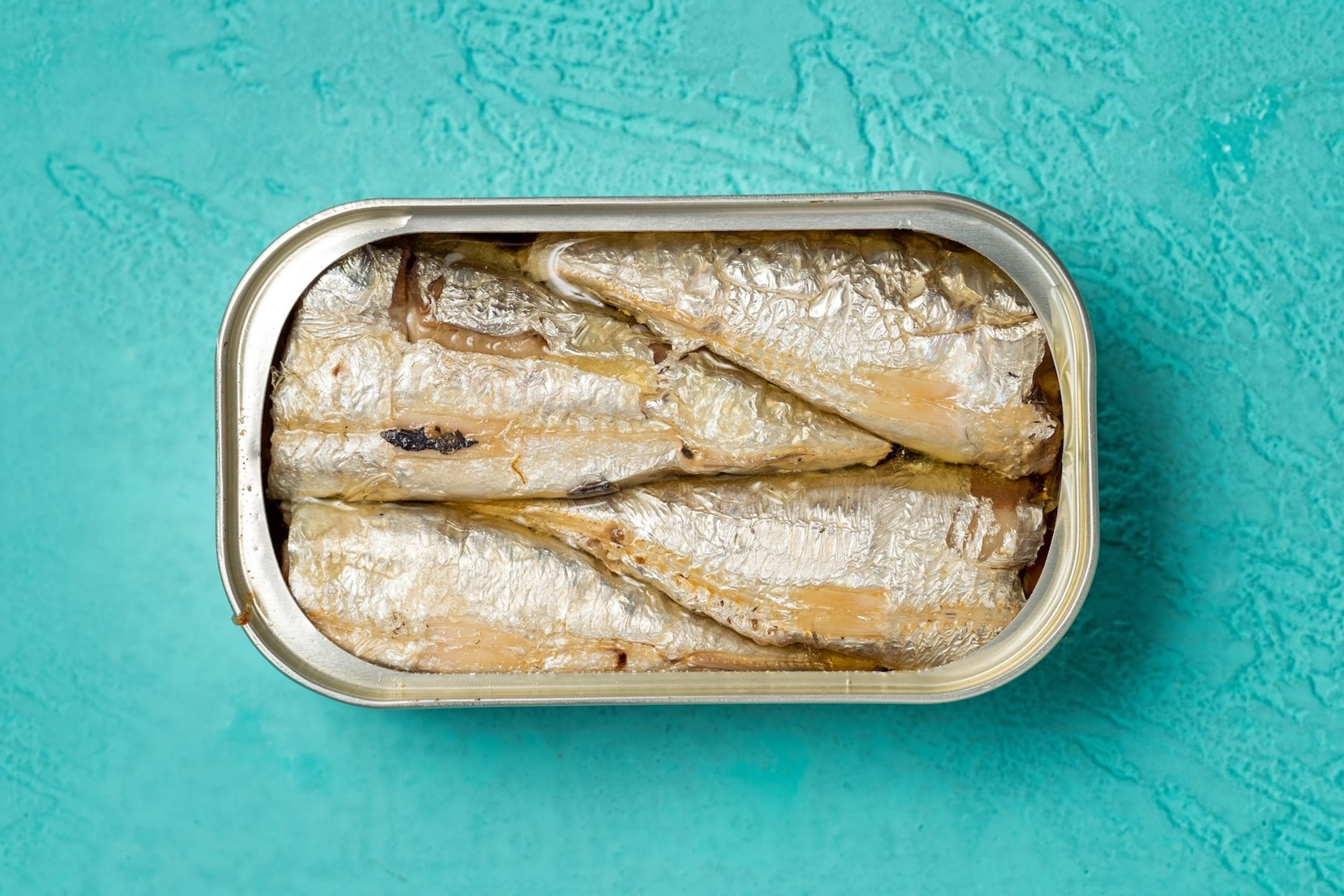 A tin of sardines (a high-protein snack) on a teal background.