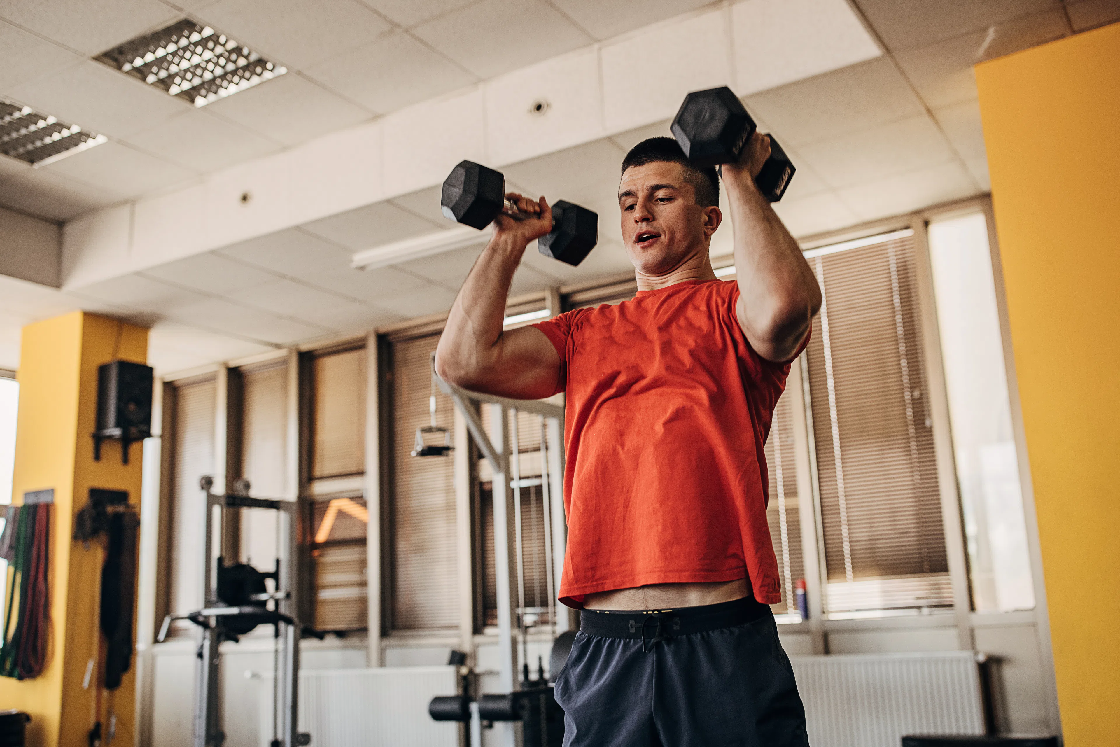 Man doing the thrusters exercise with dumbbells in a gym.
