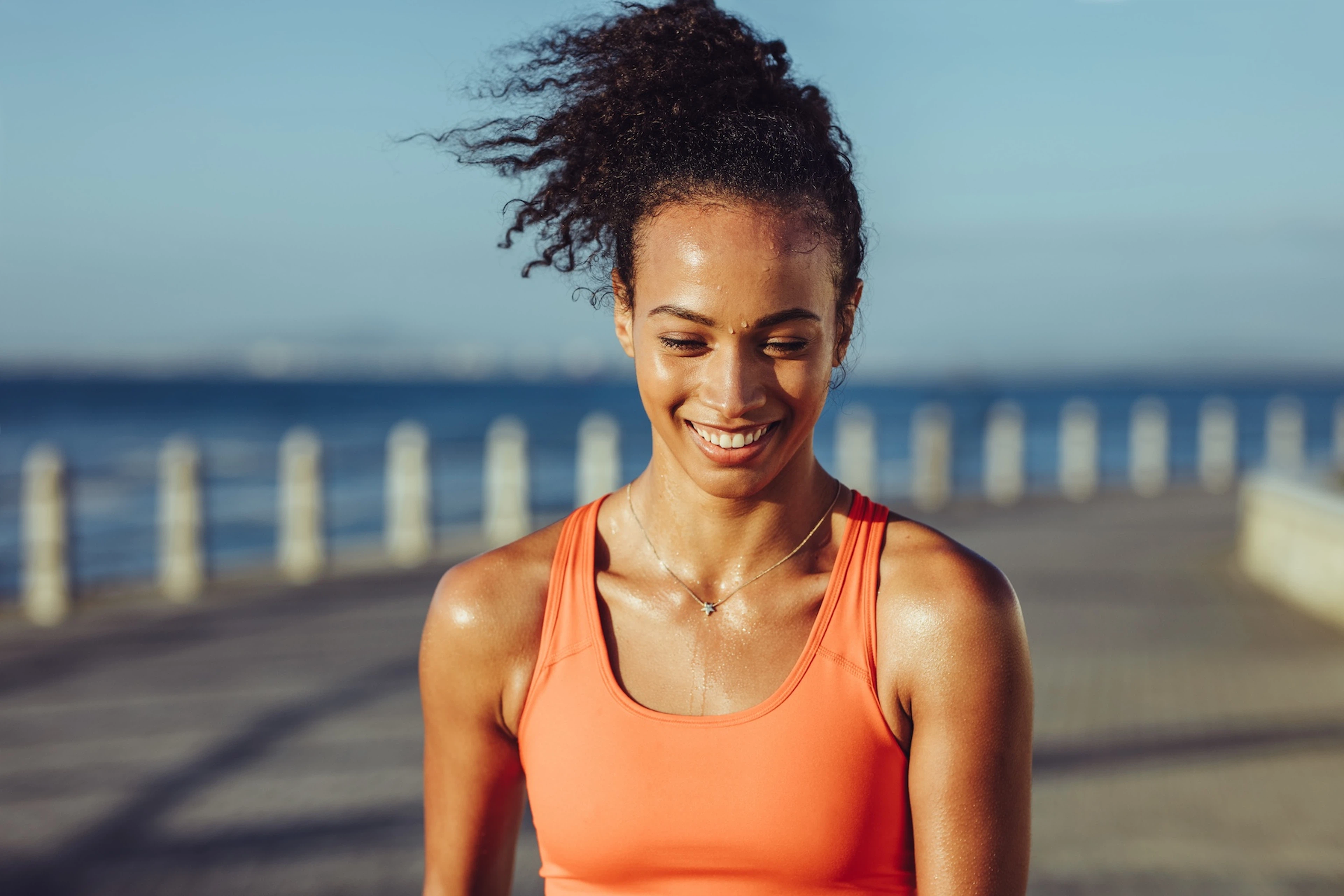 A happy, sweaty athlete looking down and smiling while going for an outdoor walk on a sunny day.