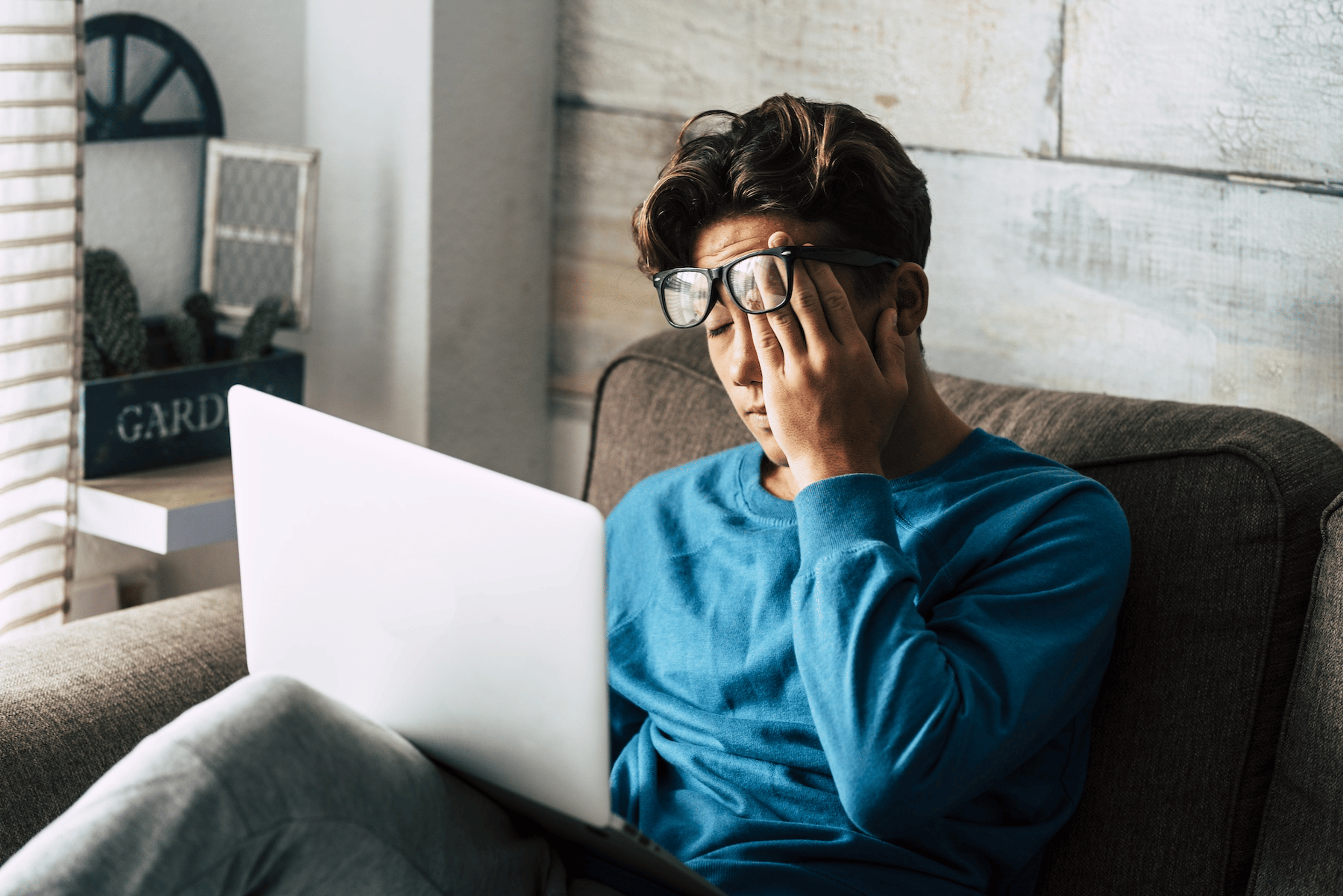 A student rubbing their eyes while working on a laptop at home. They are feeling tired even after a full night of sleep.