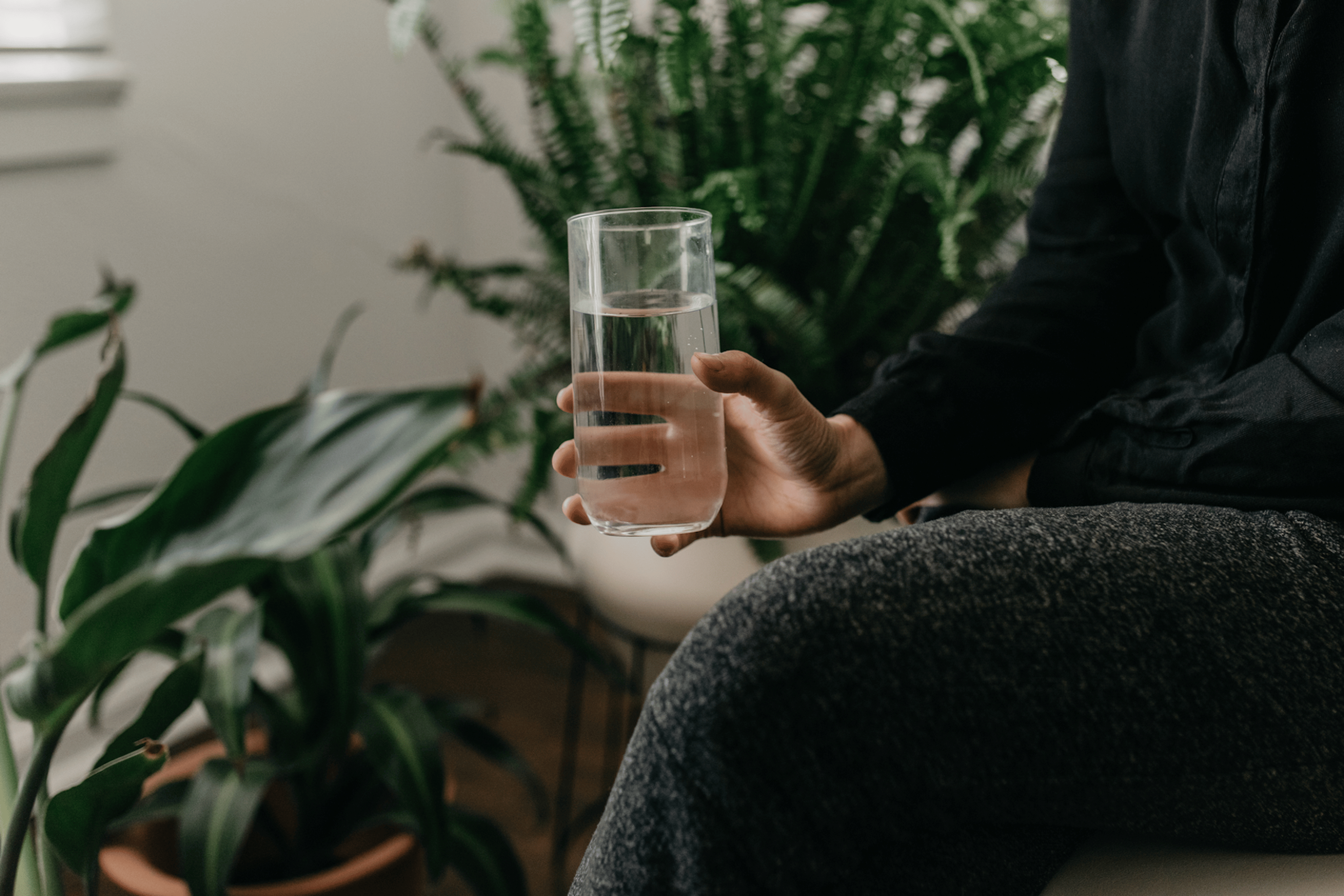 A close-up image of a person in comfy clothes holding a glass of water, drinking water before bed.