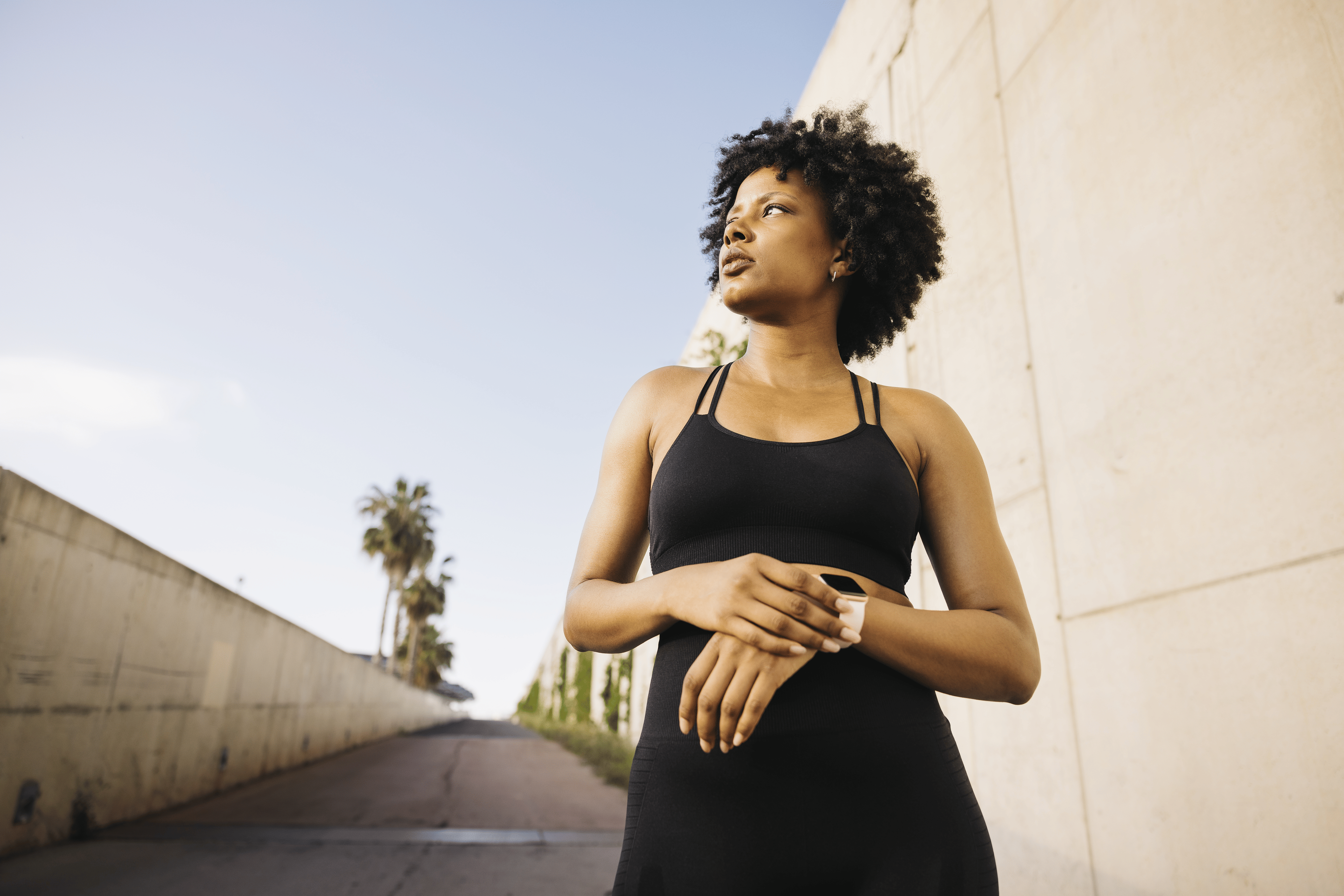 A young woman outside in workout clothes checking her smartwatch deciding whether to run faster or longer