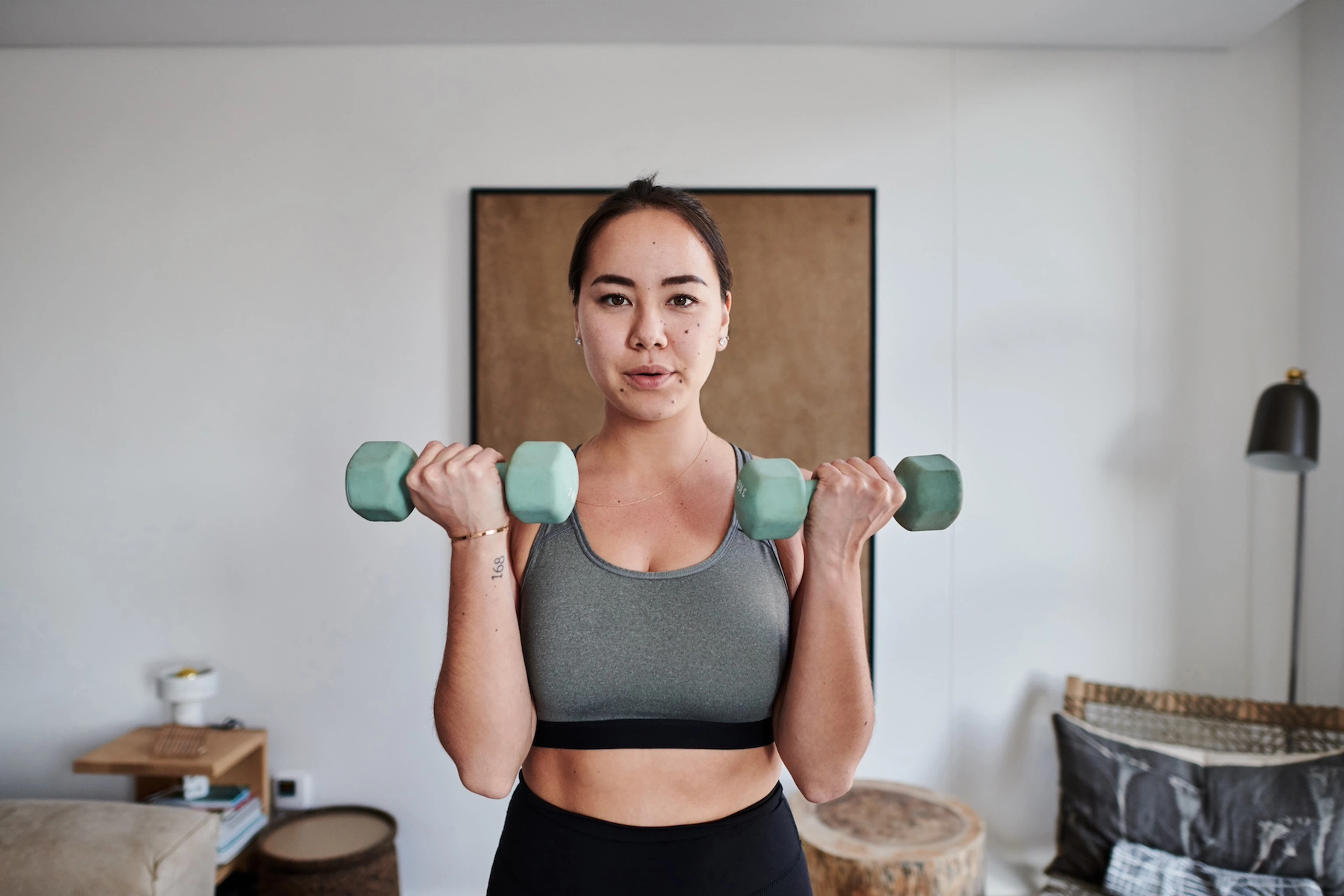 A woman lifting dumbbells at home while looking at the camera.