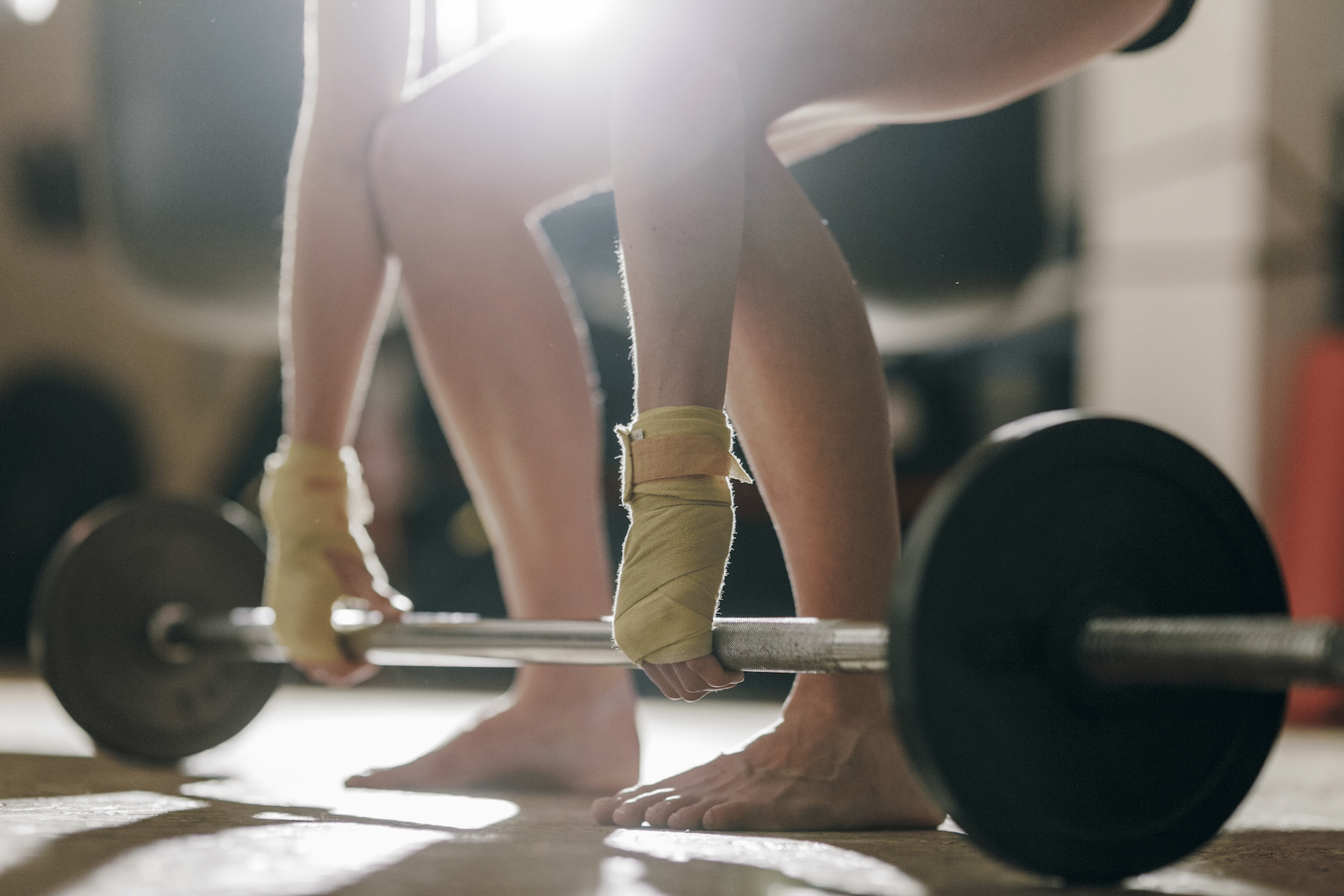 A zoomed-in photo of a woman working out barefoot. She's about to perform a deadlift with a barbell.