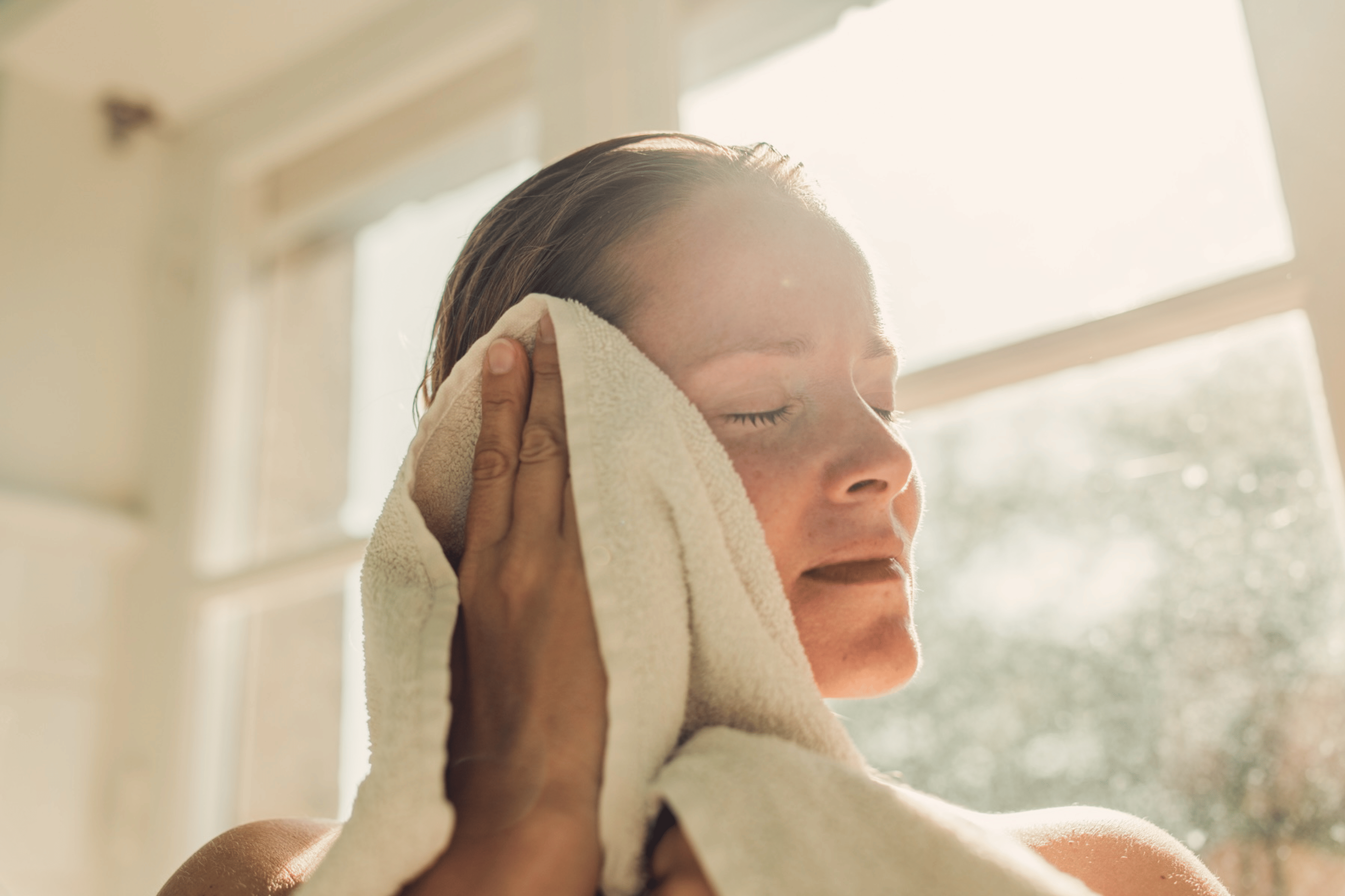 A woman drying her face with a towel as she's sweating after a shower.