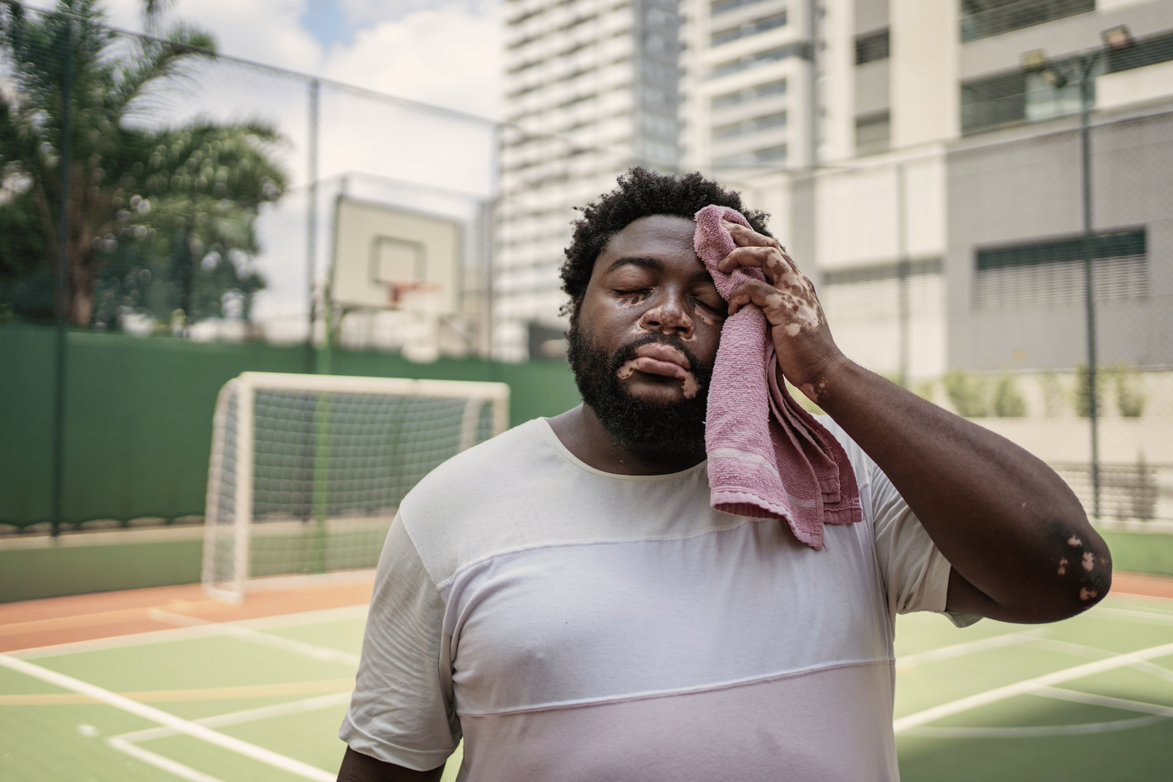 A man wiping away sweat from his face with a towel after an outdoor basketball game.