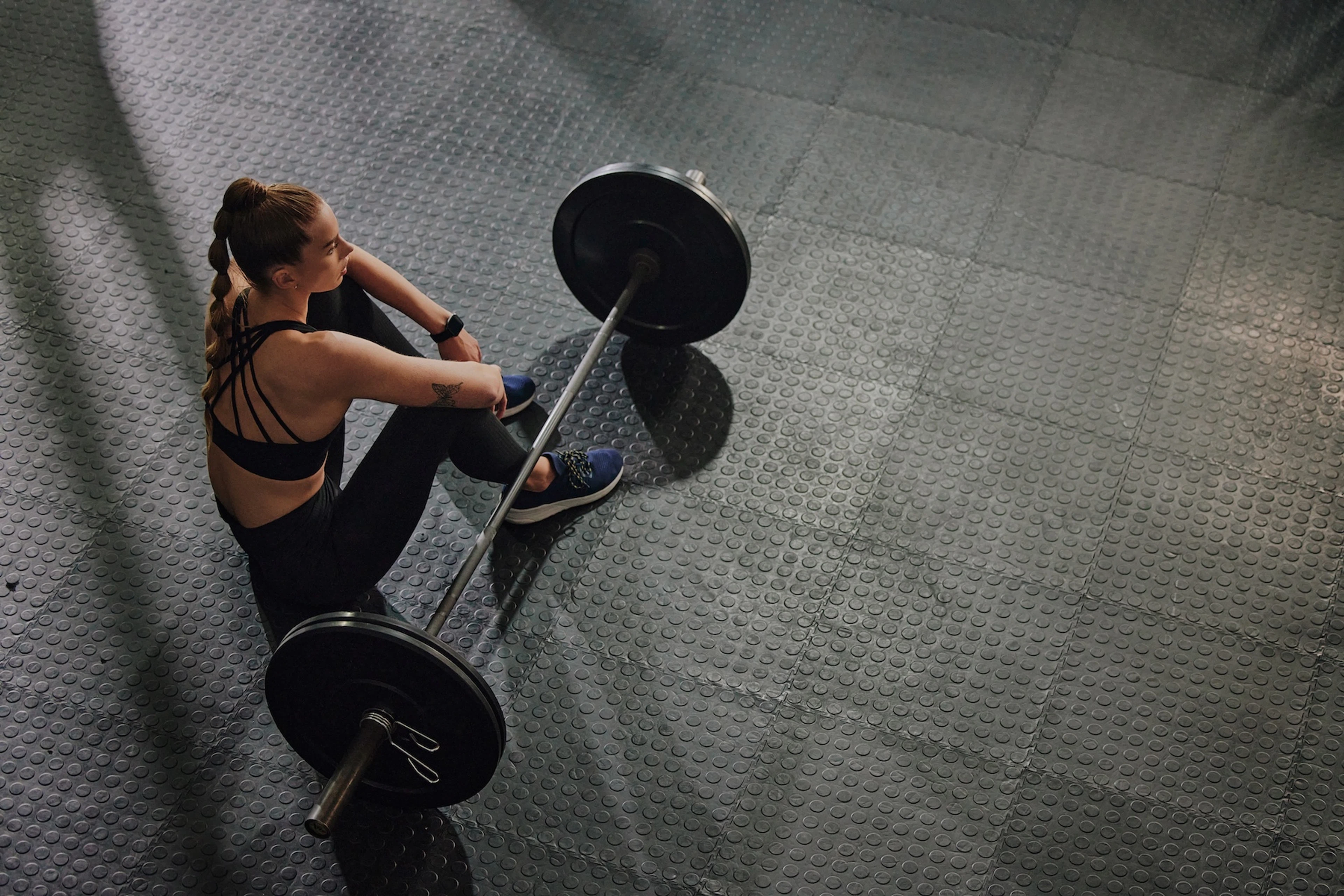A woman sitting on the floor at the gym next to a barbell.