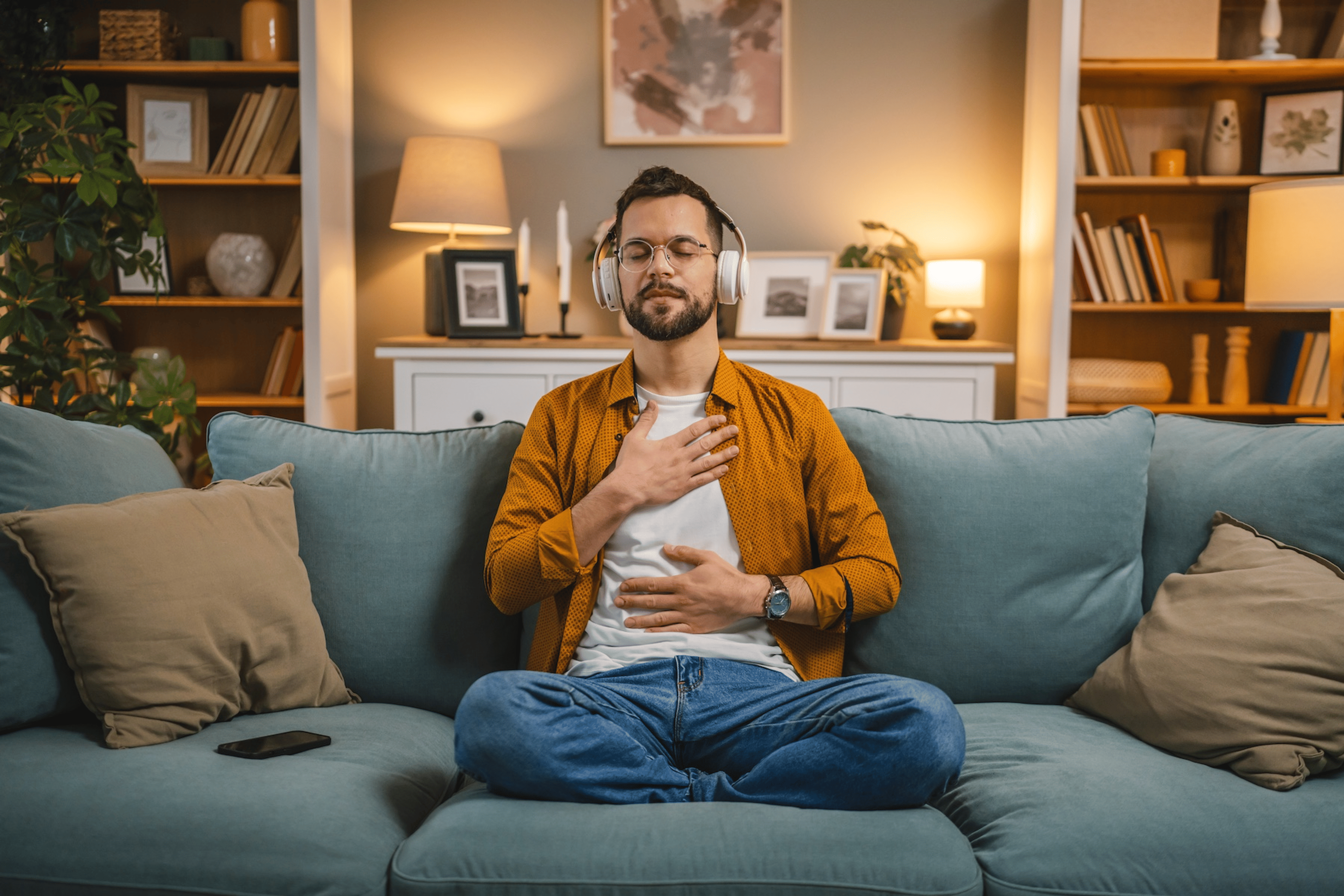  A man sitting on the couch at home with his hands on his chest and belly, practicing a loving-kindness meditation.