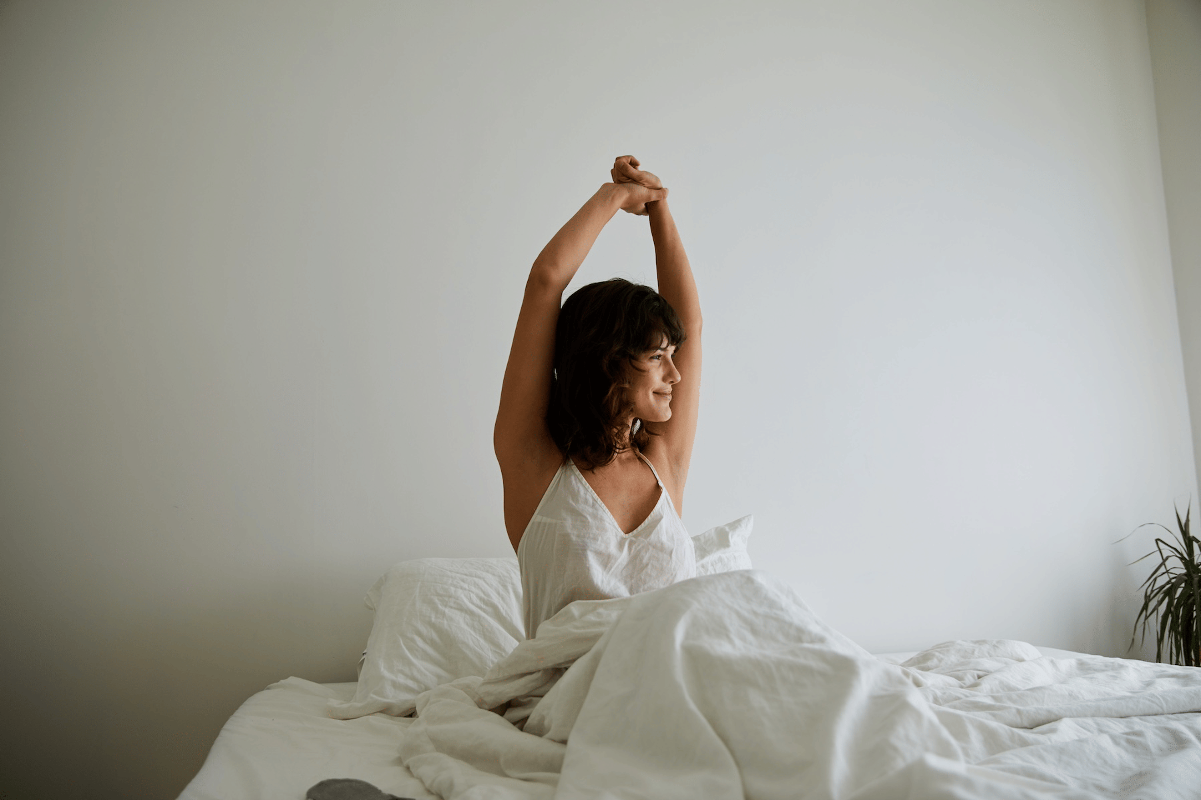 A woman stretching her arms above her head in bed after waking up.
