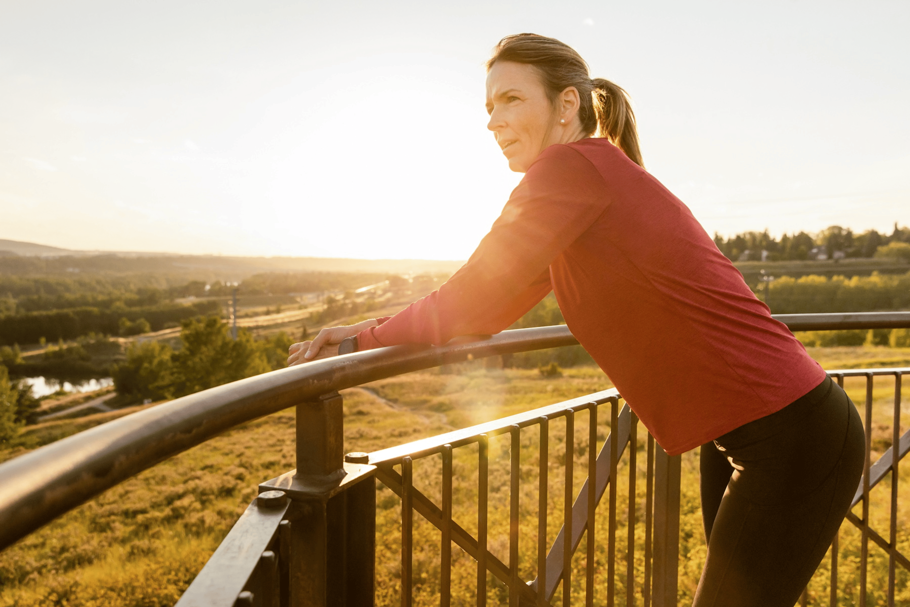 A trail runner taking a break outside and leaning against a fence as she listens to her body.