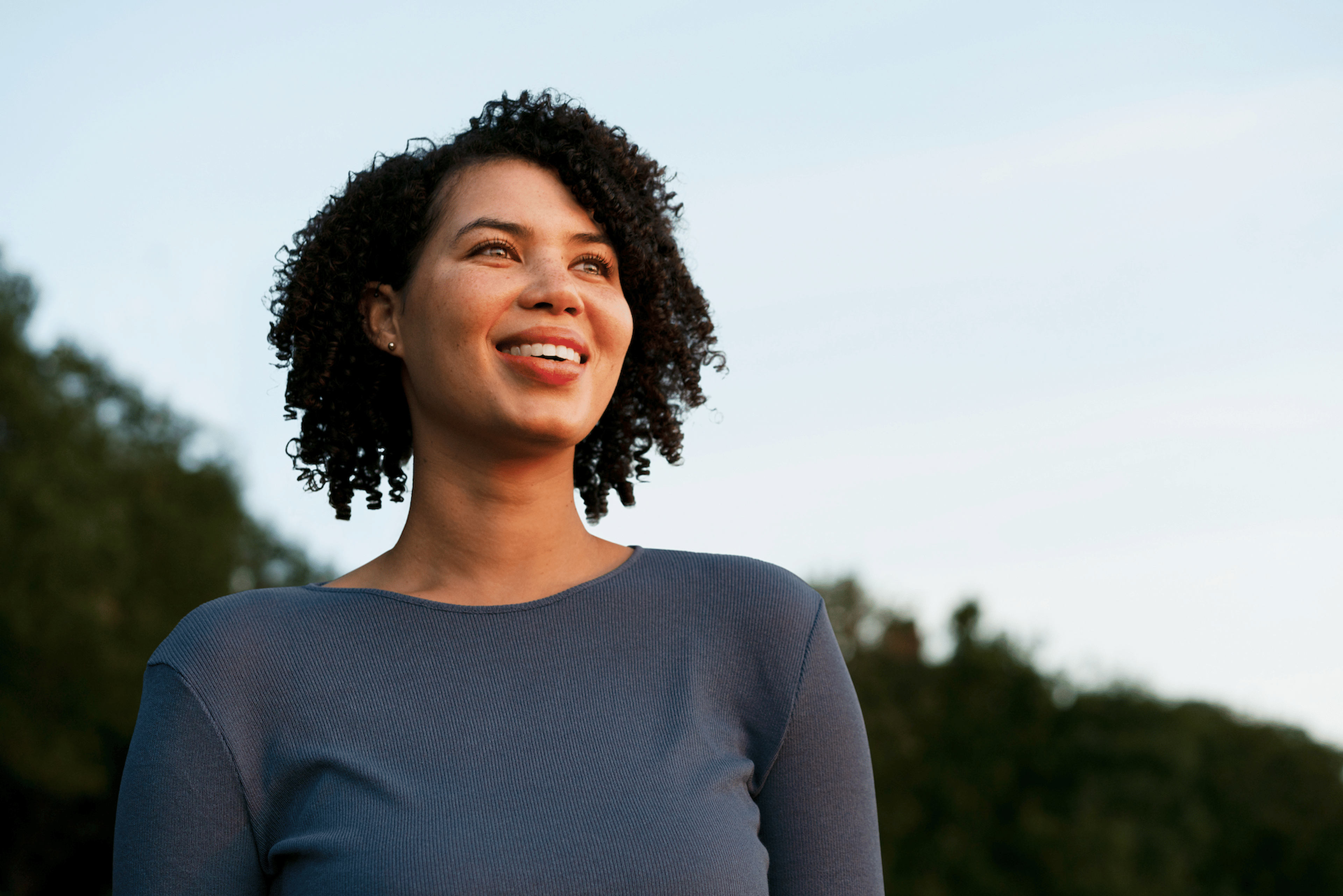 A woman looking into the distance smiling outdoors while setting intentions.