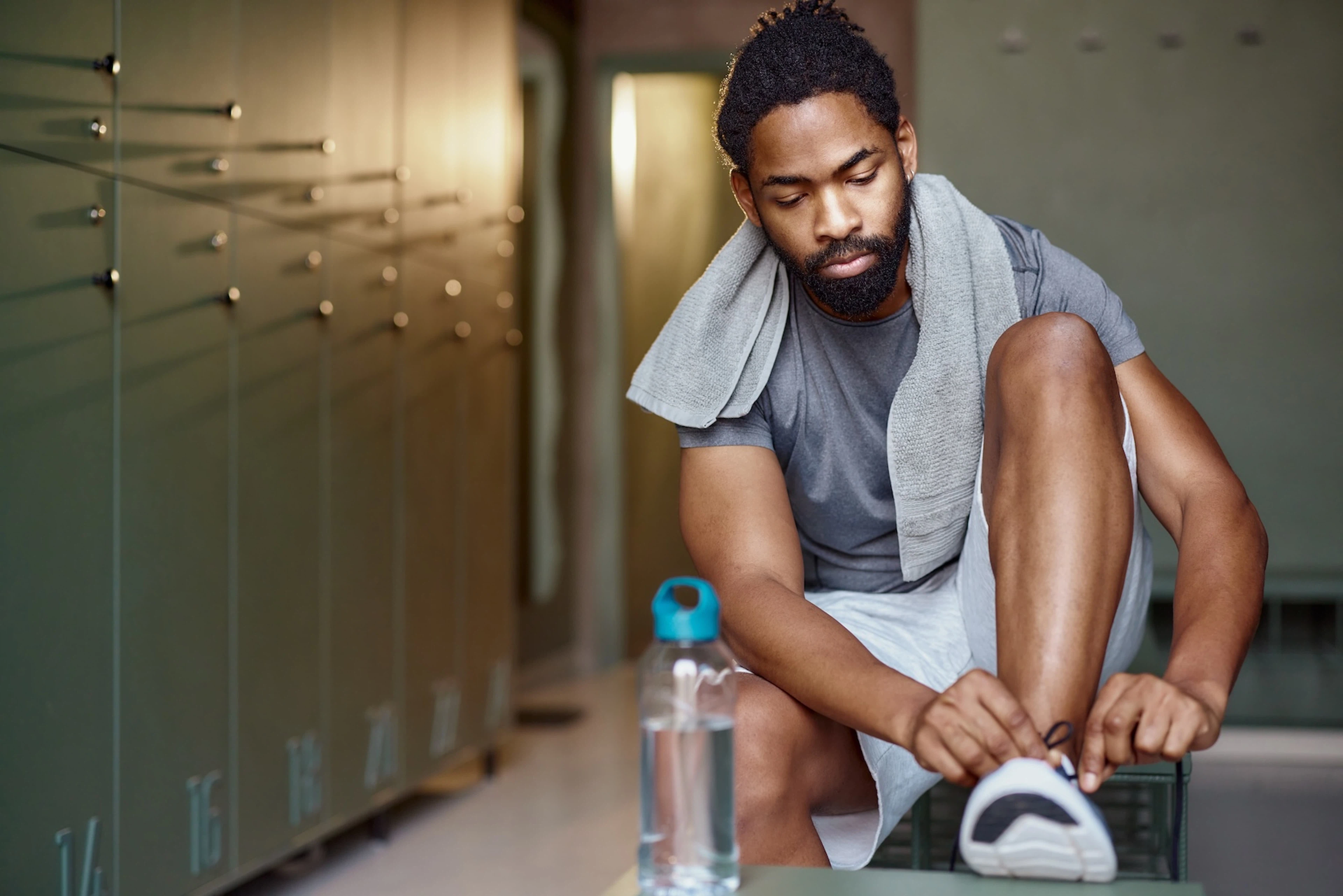 A man lacing up his running shoes in a locker room before going to work out.