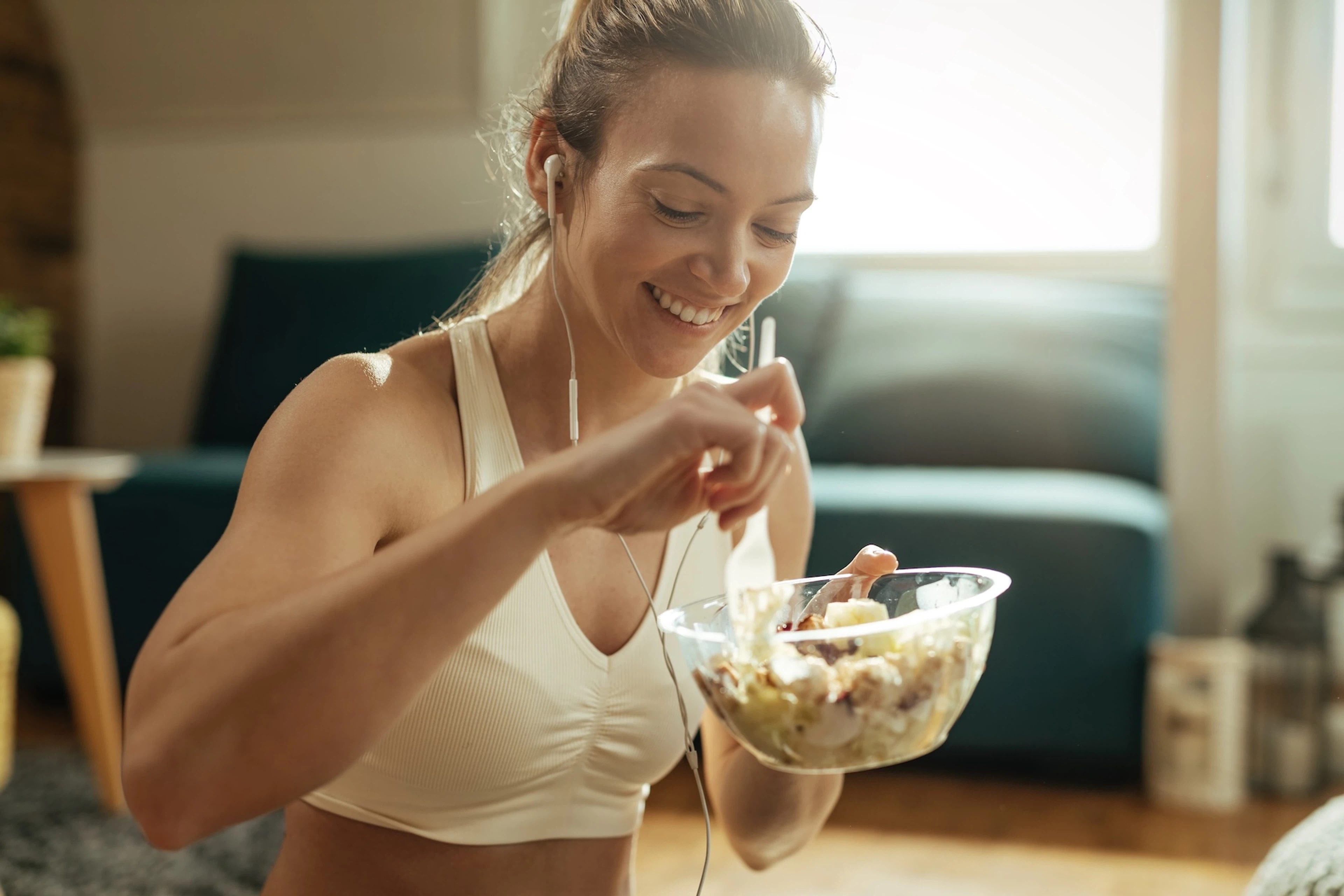 A smiling woman eating a salad after a workout.