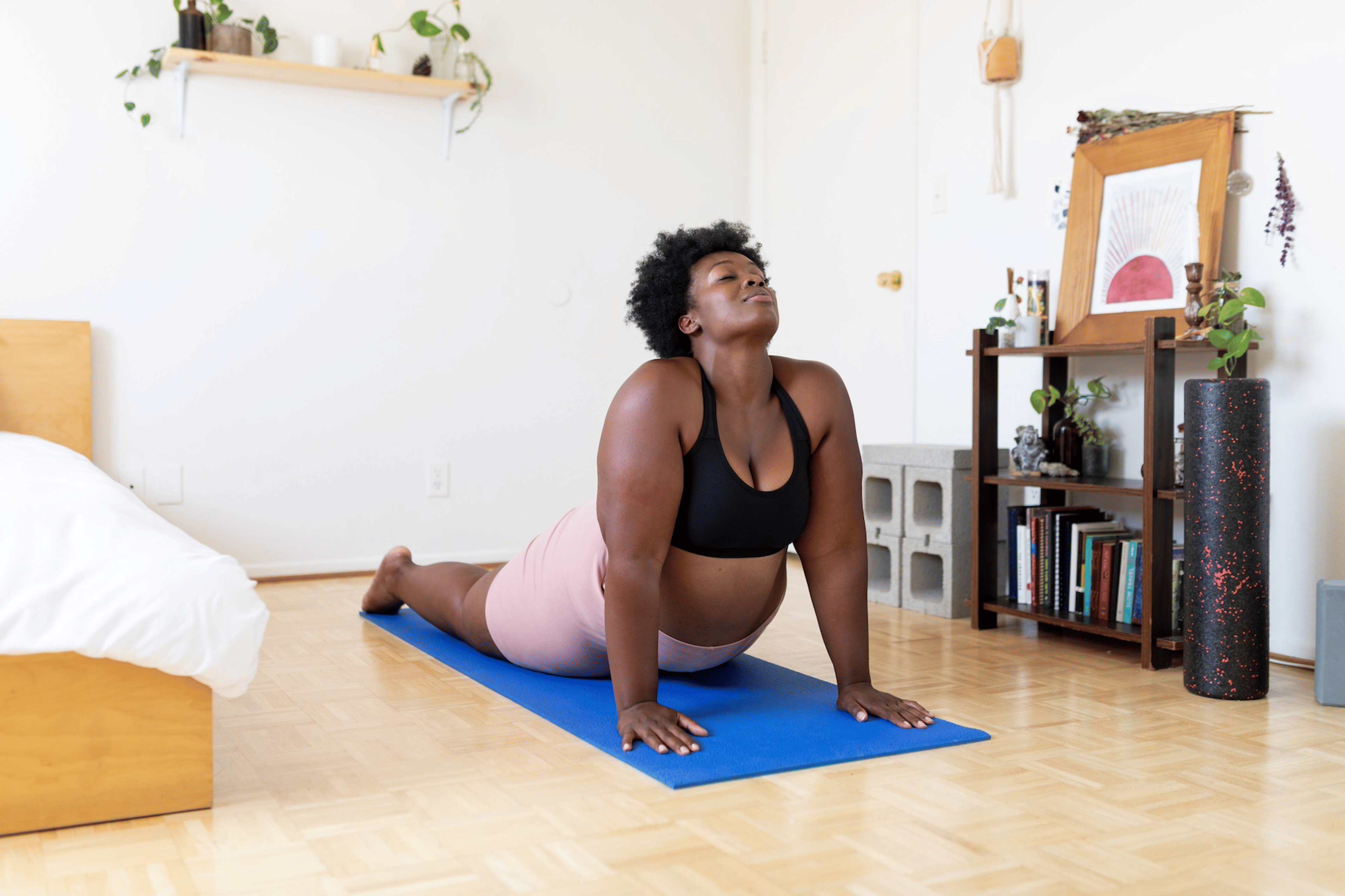 A woman doing cobra pose on a yoga mat in her sunny bedroom to strengthen her mind-body connection.