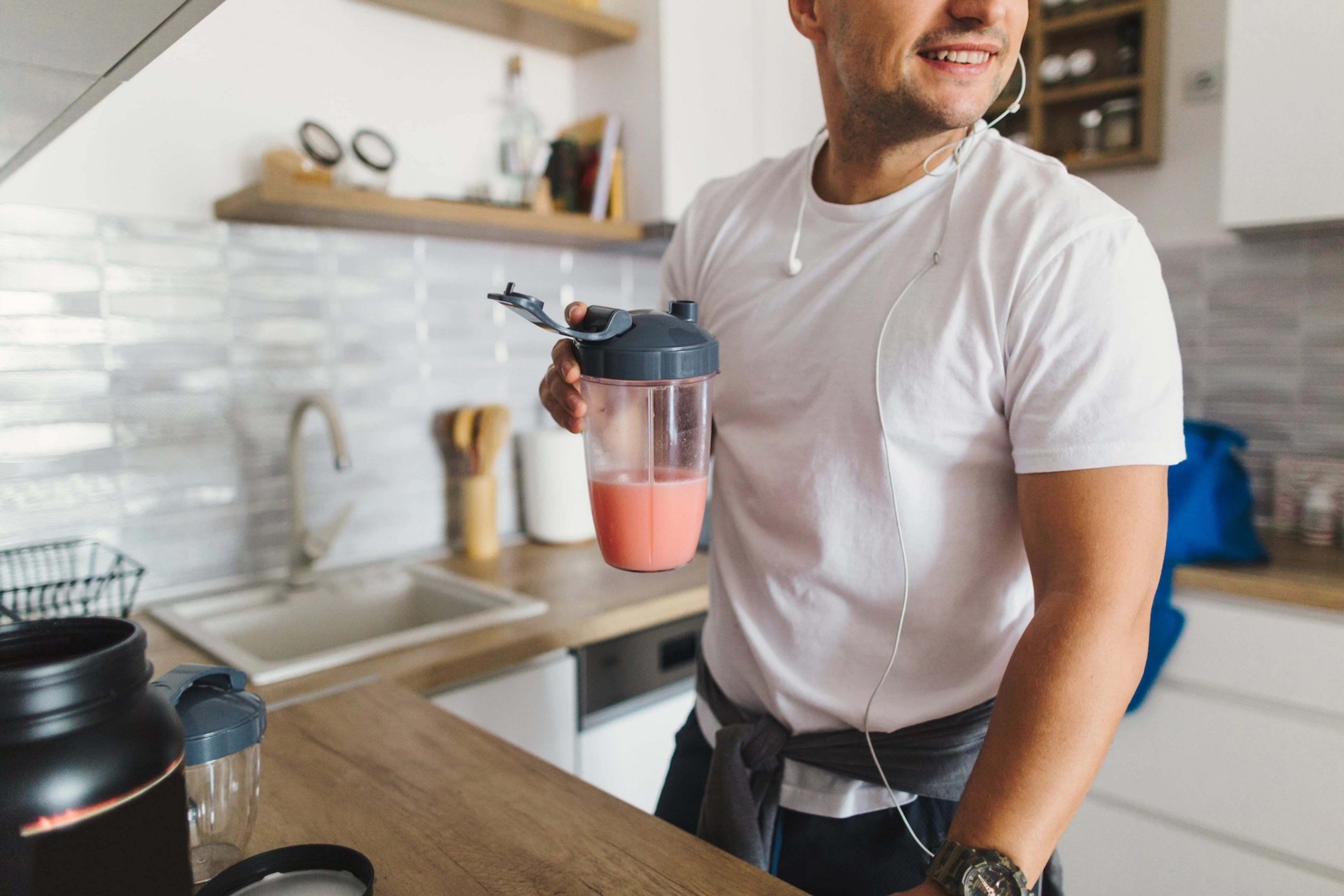 A close-up photo of a man drinking a smoothie in his kitchen, a great post-workout recovery drink.
